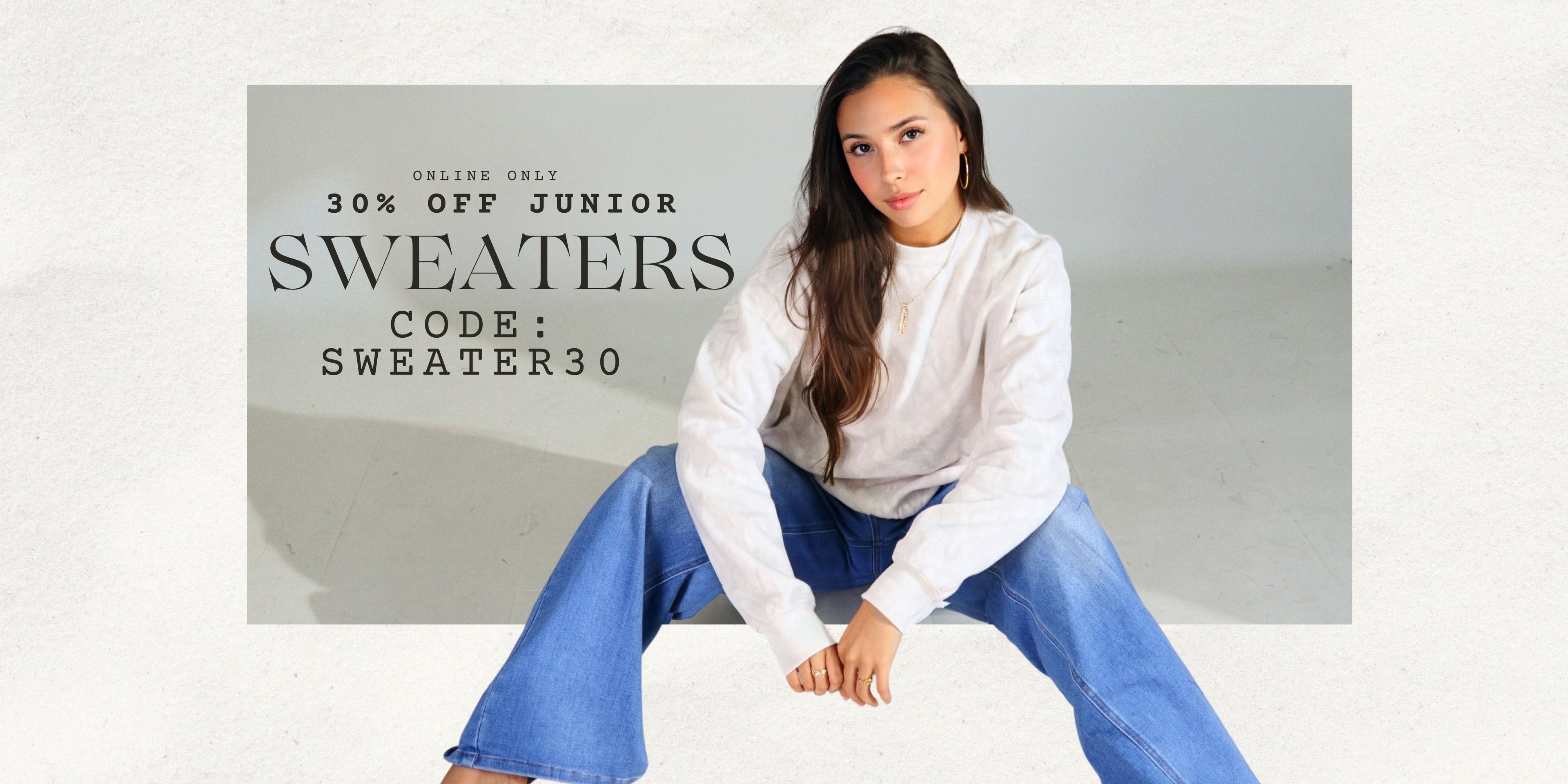 Woman sitting on a white surface with promotional text for junior sweaters on a gray background. Online only, 30% off junior sweaters. Use code: SWEATER30