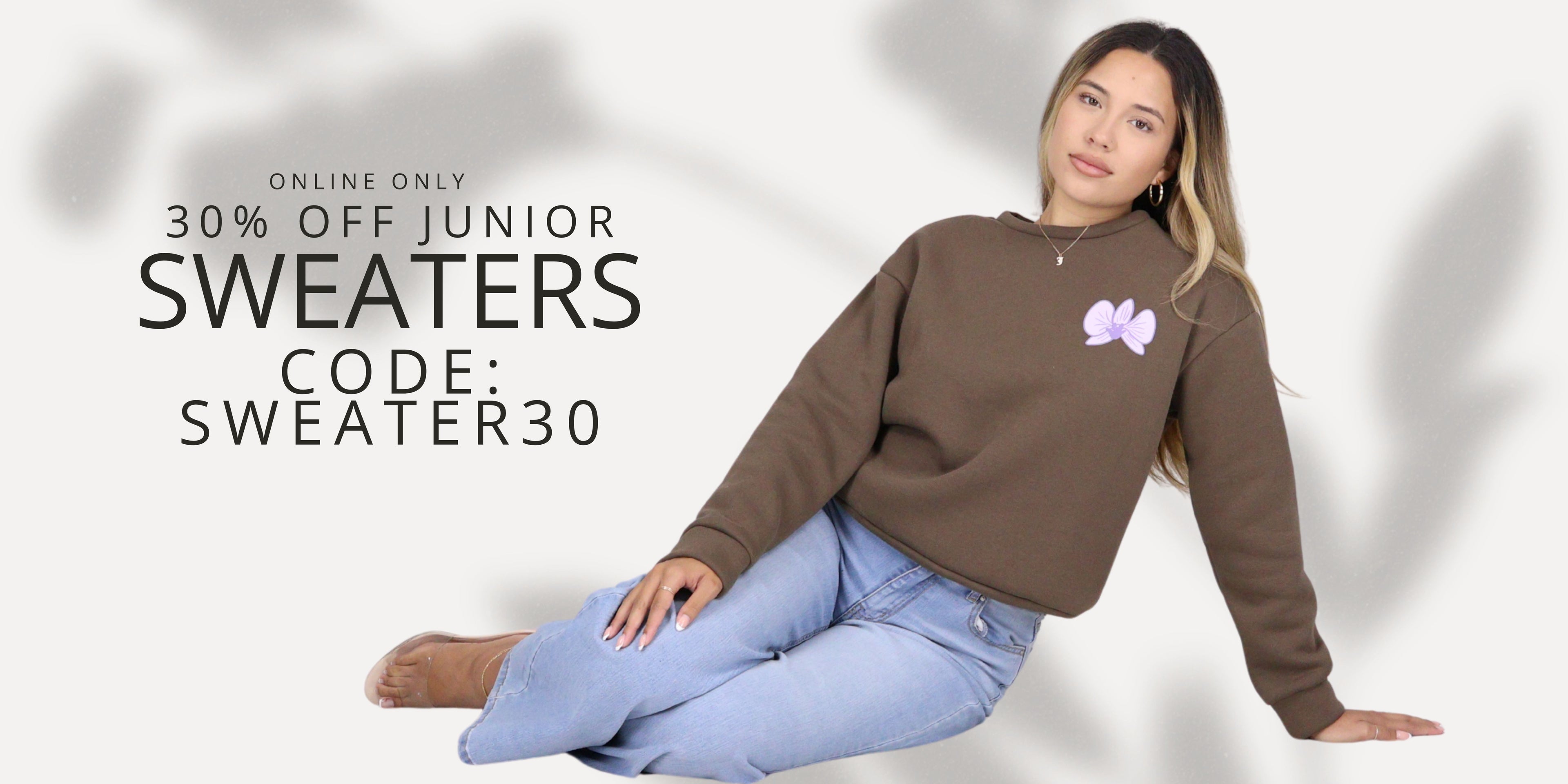 Woman wearing a brown sweater with a logo, sitting on the floor against a white background with promotional text for junior sweaters. Use promo code: SWEATER30