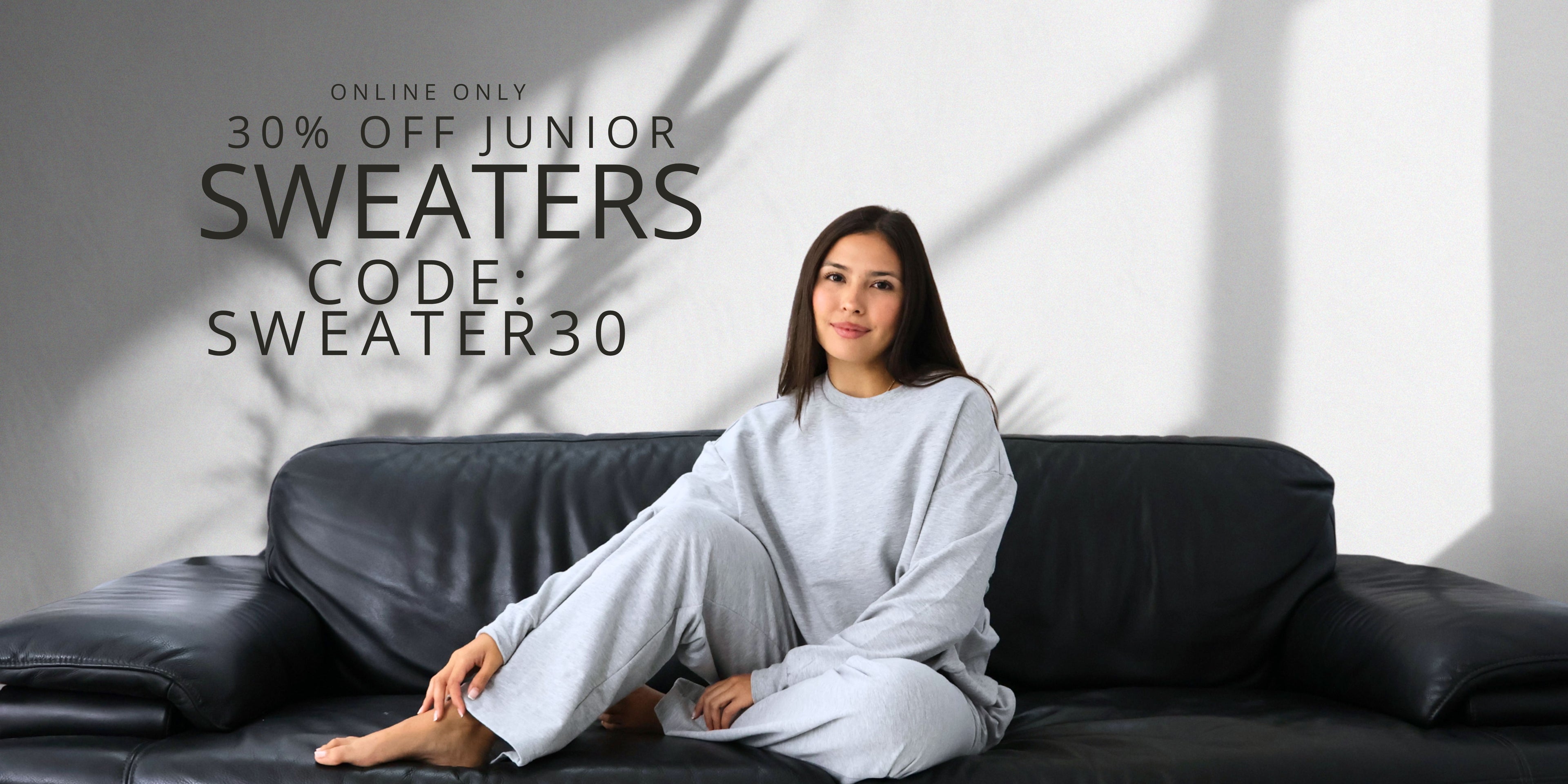 Woman sitting on a black couch wearing a gray sweater and pants with promotional text overlay. Online only, 30% junior sweaters. Use code: SWEATER30
