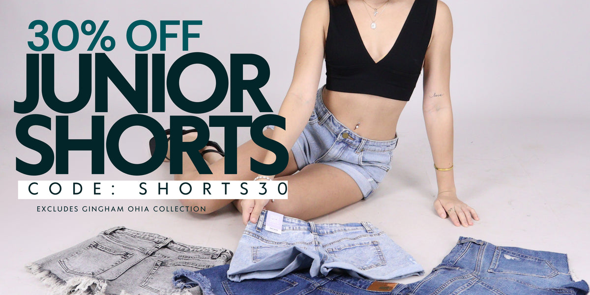 A promotional banner for 'Junior Shorts' showing a model sitting on a light gray floor wearing denim shorts, with other denim shorts laid out in front of her. Large text on the left reads '30% OFF JUNIOR SHORTS', 'CODE: SHORTS30', and 'Excludes Gingham Ohia Collection'.