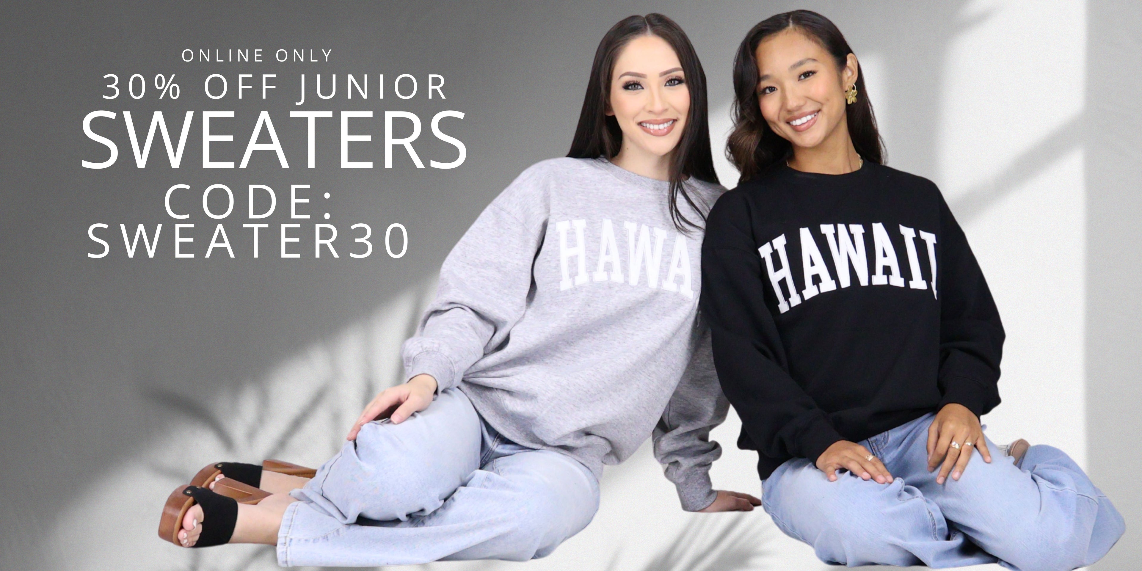 Two women sitting next to each other wearing sweater with Hawaii printed on top with promotional text. Online only 30% off junior sweaters. Use code: SWEATER30